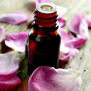 Essential oil with rose petals on wooden background