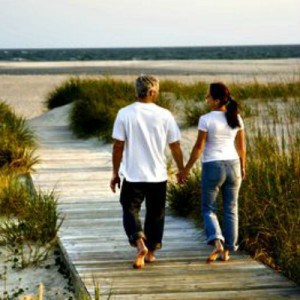 Back view of mid-adult Caucasian couple walking down walkway to beach.